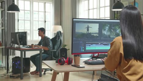 back view of asian female video editor celebrating while works with footage and sound on her personal computer in office