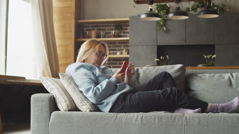 Rothaarige-Frau,-Die-Mit-Dem-Handy-Auf-Dem-Sofa-Liegt