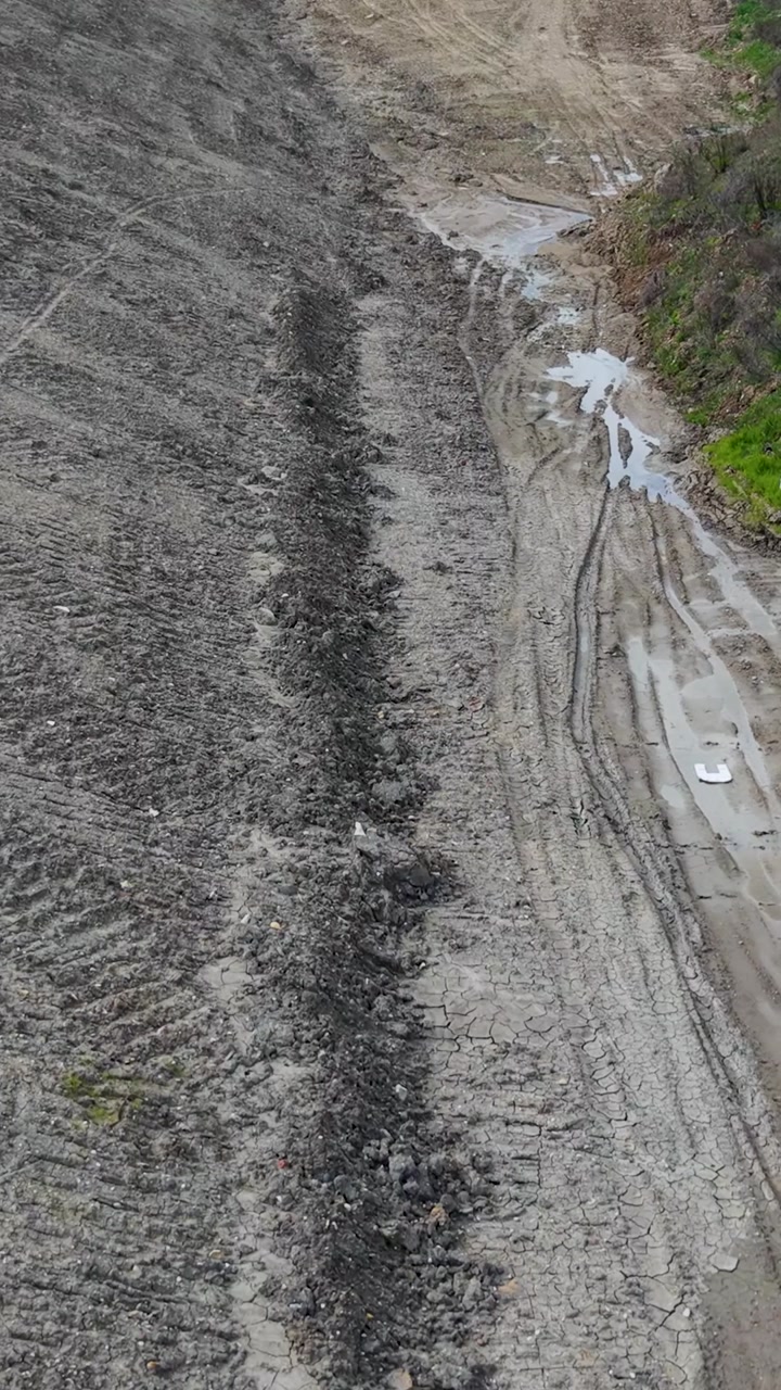 Vertical drone flight through Panshanger quarry valley, Hertfordshire, England. Low forward aerial pass over muddy tracks, gravel slopes, puddles and exposed earth in an active excavation landscape.