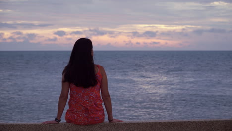 mujer joven admira la puesta de sol sobre el mar con impresionantes nubes púrpuras dramáticas en las noches de verano
