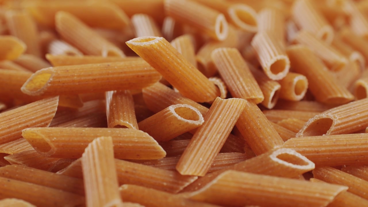 Pasta integrale biologica, maccheroni di semola di grano duro, penne rigate crude in una ciotola di legno. Filmato 4k di alta qualità