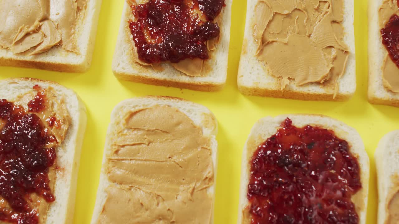 Close up of multiple peanut butter and jelly sandwiches on yellow surface
