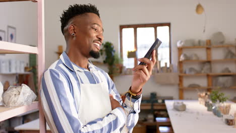 Happy-african-american-man-with-beard-talking-on-phone-and-smiling-in-pottery-studio,-slow-motion