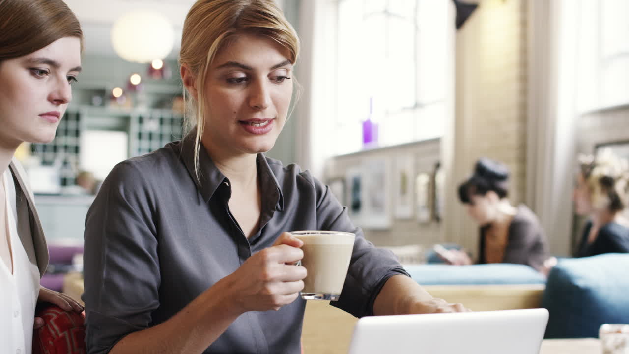Forretningskvinner møtes på kafé, bruker laptop og drikker kaffe.