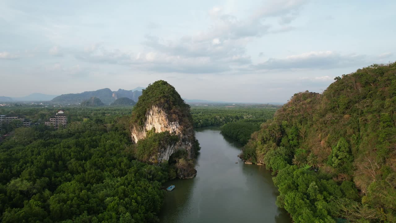 Flycam bay lùi hé lộ một dòng sông chảy giữa hai ngọn núi đá vôi lớn màu xanh ở thị trấn Krabi, Thái Lan vào một buổi chiều hoàng hôn.