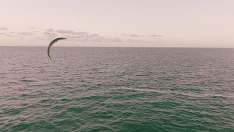 Aerial-dolly-in-of-skilled-person-doing-kite-boarding-in-turquoise-sea-at-golden-hour-near-Miami-Beach-shore-and-resorts,-Florida,-USA