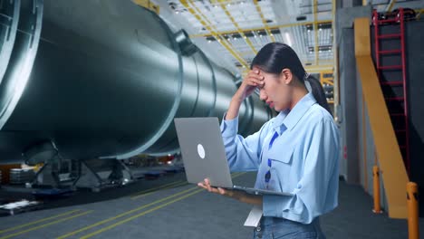 side view of woman not satisfied and shakes her head while using laptop computer in pipe manufacturing factory