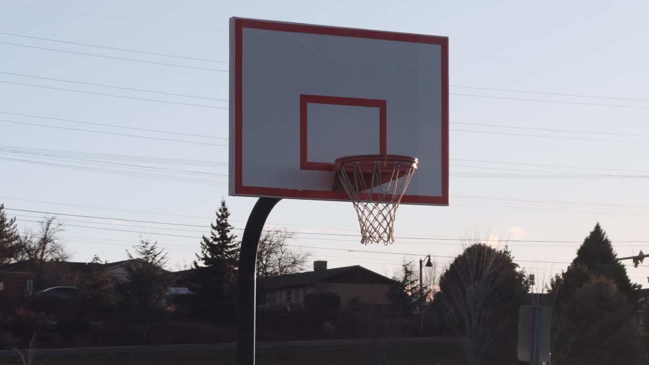 Inquadratura statica di un canestro da basket all'aperto con auto che passano sullo sfondo in lontananza