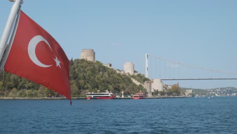 Turkish-flag-stern-of-Bosphorus-Cruise-boat,-Rumeli-castle-backdrop