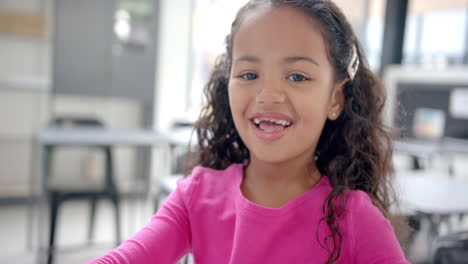 in school, young biracial girl wearing pink is smiling in the classroom