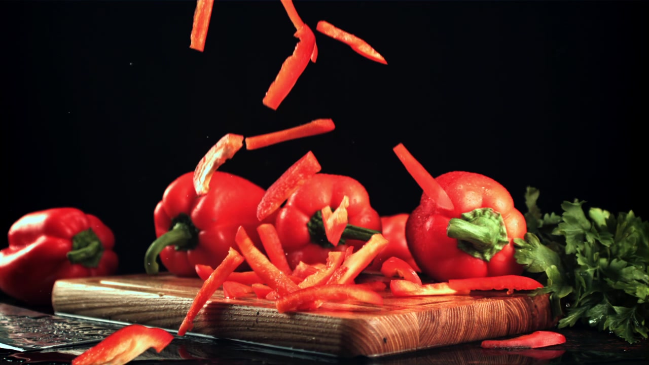 Nakrájená červená paprika padající na dřevěné prkénko ve zpomaleném záběru