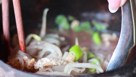 detailed view of noodle dish with chopsticks and spoon in a coconut shell bowl.