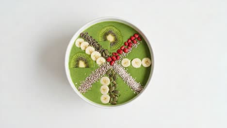 a vibrant green smoothie bowl decorated with kiwi, bananas, and pomegranate seeds presenting an eye-catching mix of healthy ingredients and aesthetic appeal