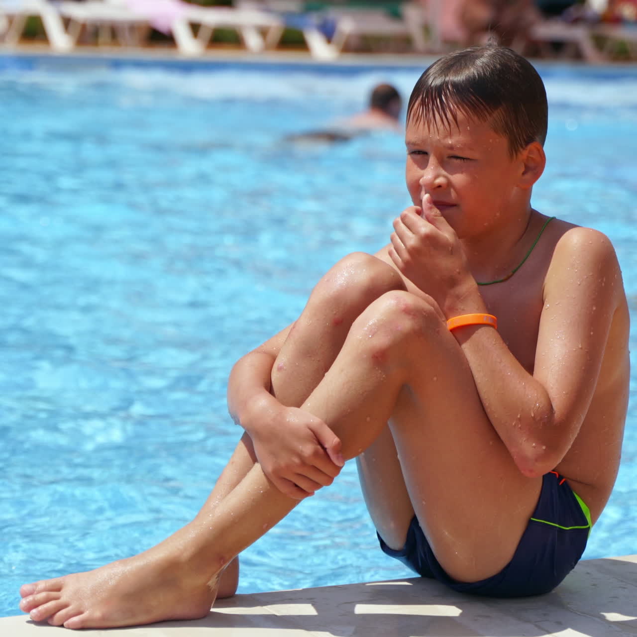 Cute boy near the swimming pool outdoors. Boy falling into the water of the pool in a sunny summer day. Joyful summer in water.