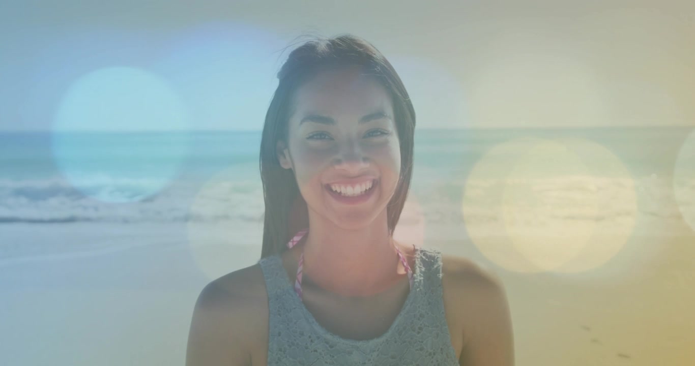 Kvinde vender mod kameraet på en solrig strand, sollys-bokeh bevæger sig hen over ansigtet, smilet breder sig til markedsføring.