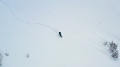 aerial view tracking a snowboarder off piste in fresh snow