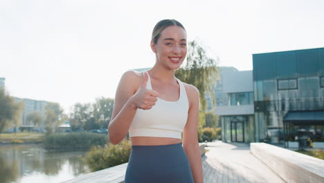 smiling athletic fit slim runner woman showing double thumbs up in sunshine city park outdoors