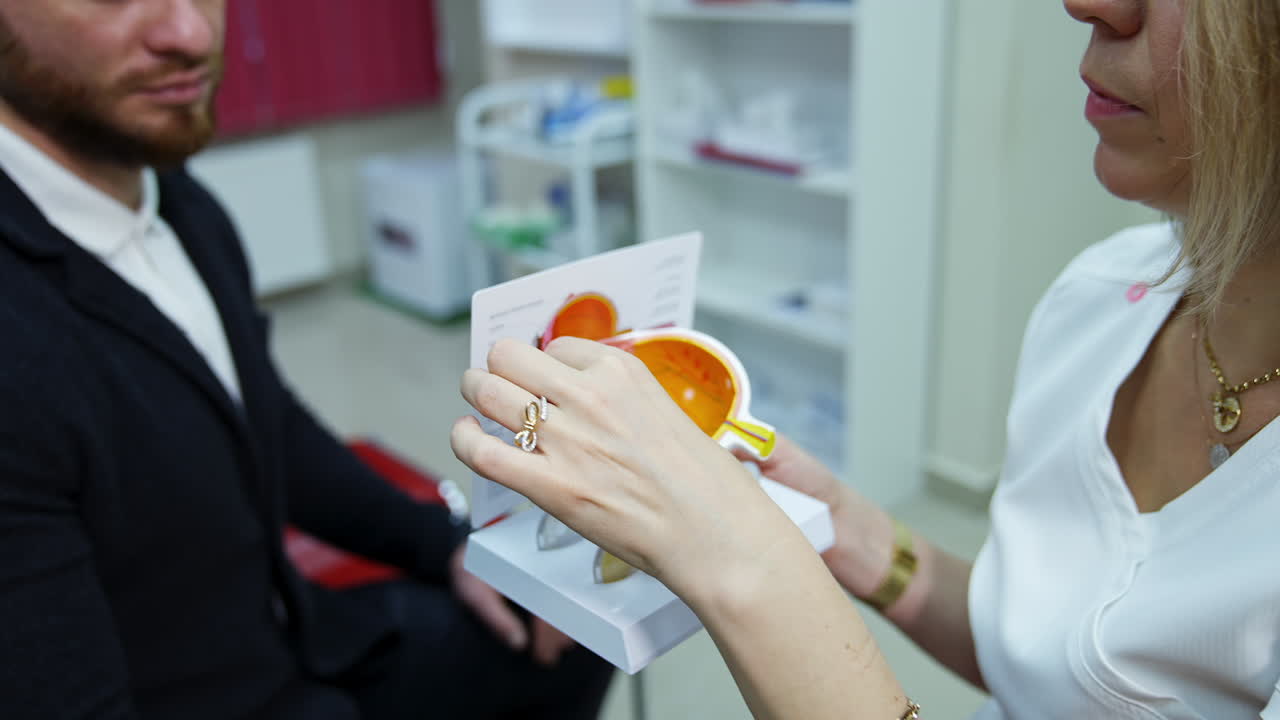 Ophthalmologist speaking to a patient. Female optometrist holding an eye layout and showing lenses to a patient in clinic.