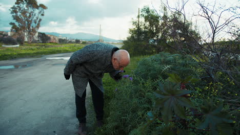 elderly man smelling a flower in a rural setting