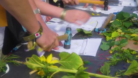 cerrar las manos de niños y adultos golpeando flores colocadas debajo de un trozo de tela para crear un arte de aspecto interesante usando pulseras de un taller de festival de música para todas las edades actividad de grupo de unidad