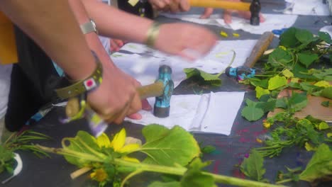 close up hands kids and adult hitting flowers placed under a piece of cloth to create interesting looking art wearing wristbands from a music festival workshop for all ages unity group activity