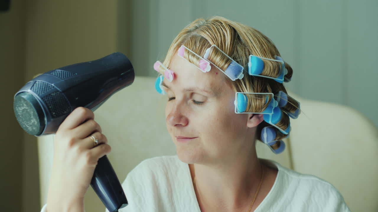 그녀의 머리에 curlers와 여자는 헤어 드라이어로 머리를 건조