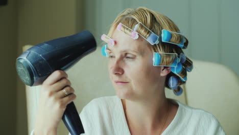mujer con rulos en la cabeza seca el cabello con secador de pelo
