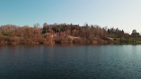 Scenic-View-Of-A-Tranquil-Lake-With-Trees-And-Houses-During-Sunset-In-Late-Winter---Annone-Lake-In-Northern-Italy---drone-pullback