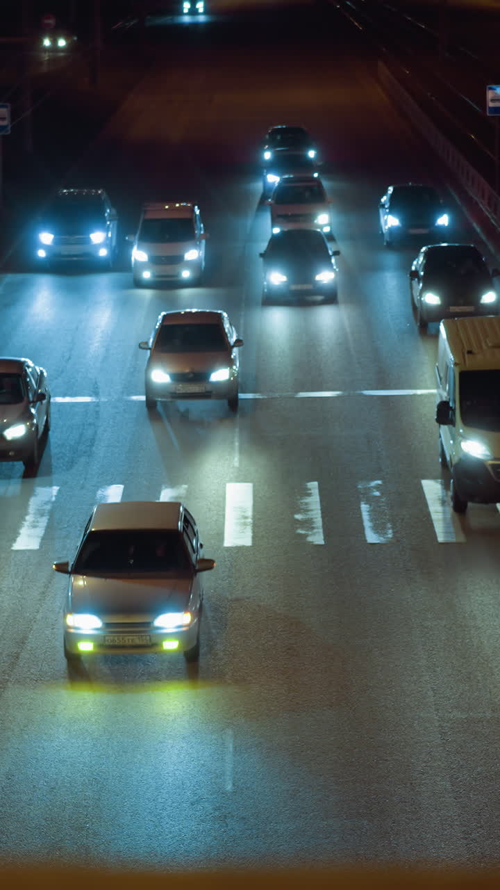 vista cercana del tráfico nocturno en un cruce de peatones con varios automóviles y sus faros iluminando la carretera, las luces de la calle y las señales para peatones son visibles