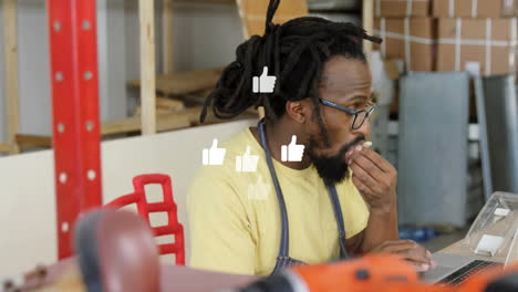 male craftsman eating snack using laptop in workshop with thumbs up icons boosting marketing