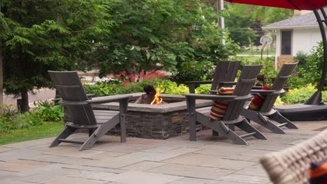 static shot of a patio seating area that includes a propane fire pit surrounded by adirondack chairs