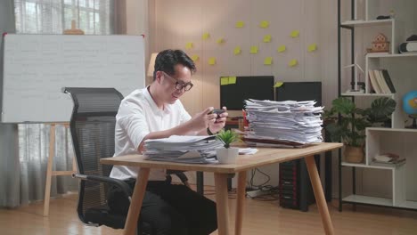 asian man enjoys playing game on smartphone after working with documents at the office