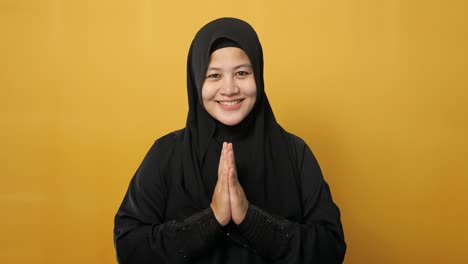 asian muslim lady smiling and shows greeting gesture against yellow background, concept of islamic celebration of ramadan or eid fitr