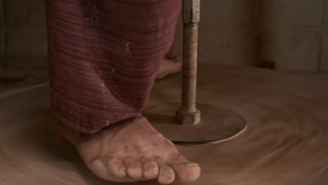 the potter rotates the wooden wheel of the potter's wheel with his feet