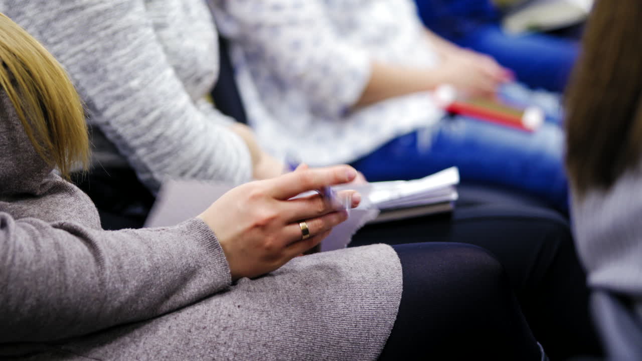Young employees are writing, sitting at working conference indoors. Women are taking notes on sheets at business meeting.
