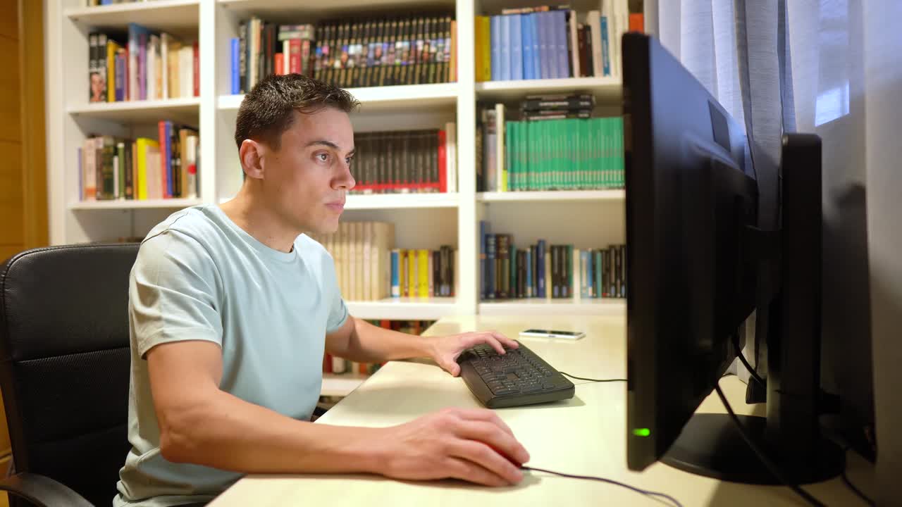 Man working on a computer at a desk in a home office with bookshelves