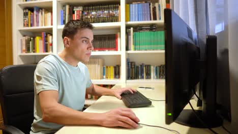man working on a computer at a desk in a home office with bookshelves
