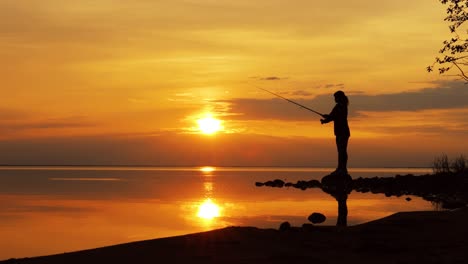 mujer pescando en una caña de pescar girando en el fondo del atardecer.
