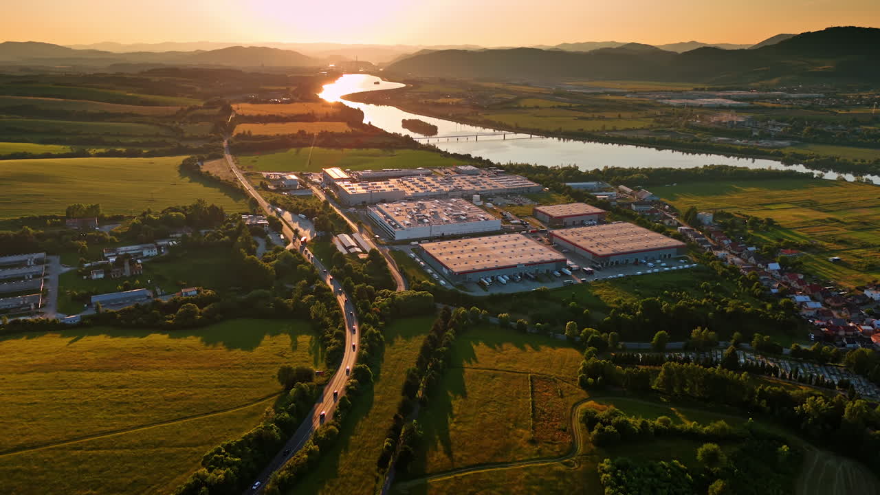 Warehouses of the industrial plant in the picturesque countryside of Slovakia. Sunset view on beautiful rural area surrounded by the Tatra mountains. Aerial view