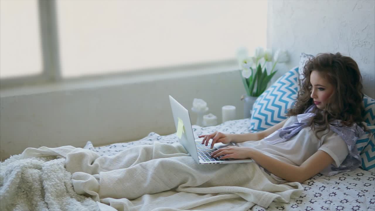 Young woman working on laptop in bed