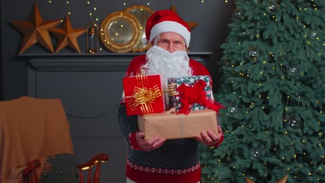 senior grandfather parodies santa claus presenting christmas gift box, holidays celebration at home