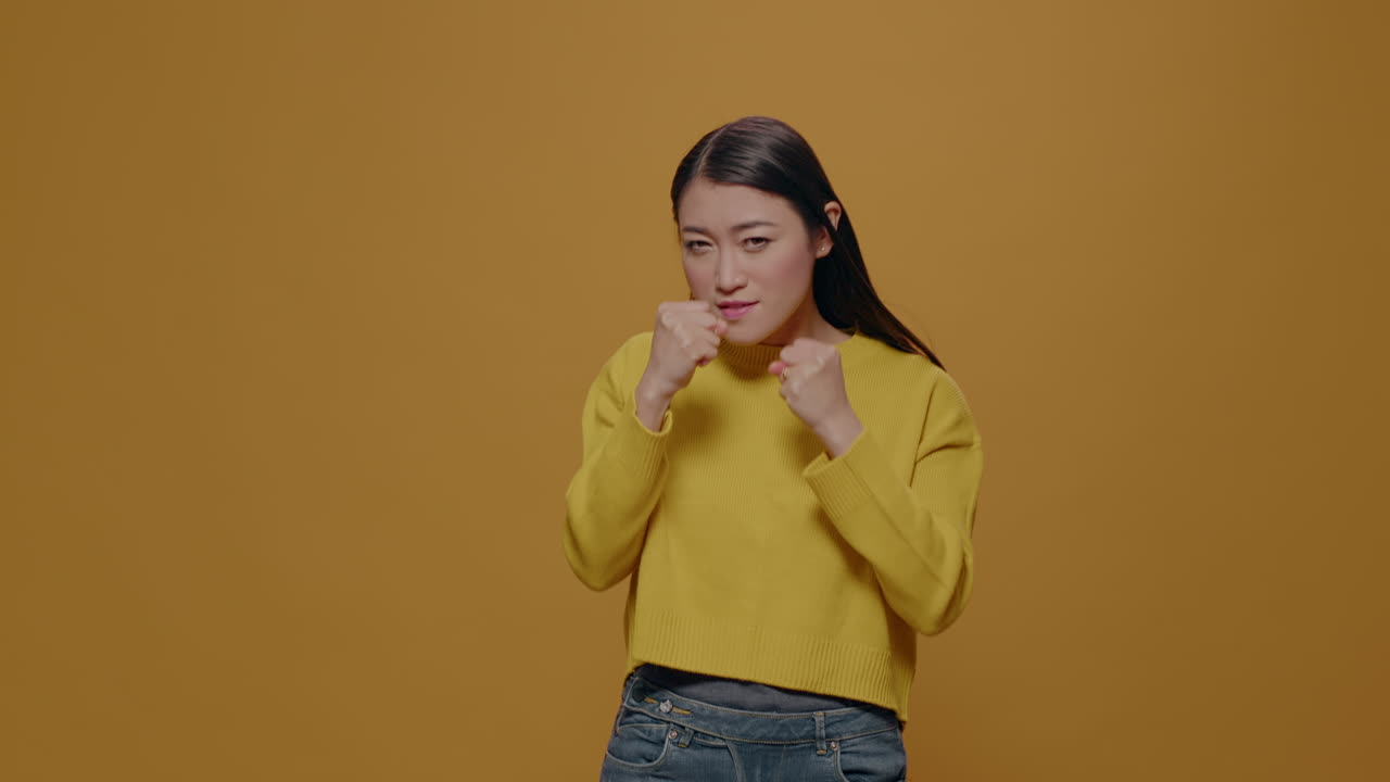 Asian woman clenching fists to punch in front of camera