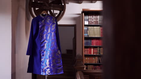 traditional blue chinese robe with gold embroidery hangs in a vintage library setting