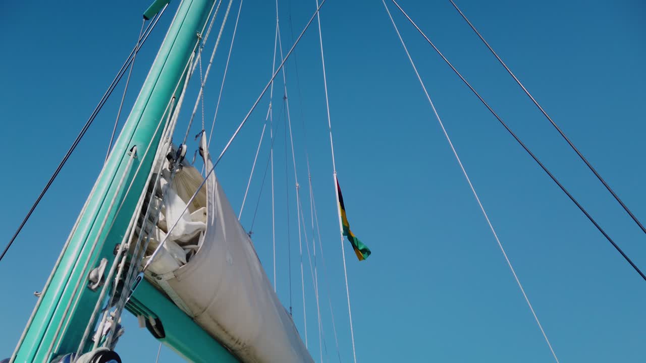 un tiro desde abajo de un mástil con muchas cuerdas rectas subiendo, y parte de la botavara con la vela se quedó