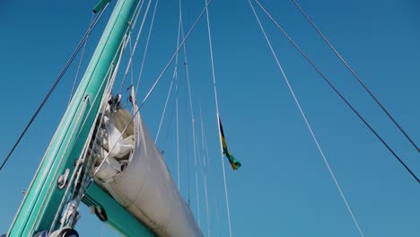 a shot from below os a mast with many straight strings going up, and part of the boom with the sail stayed