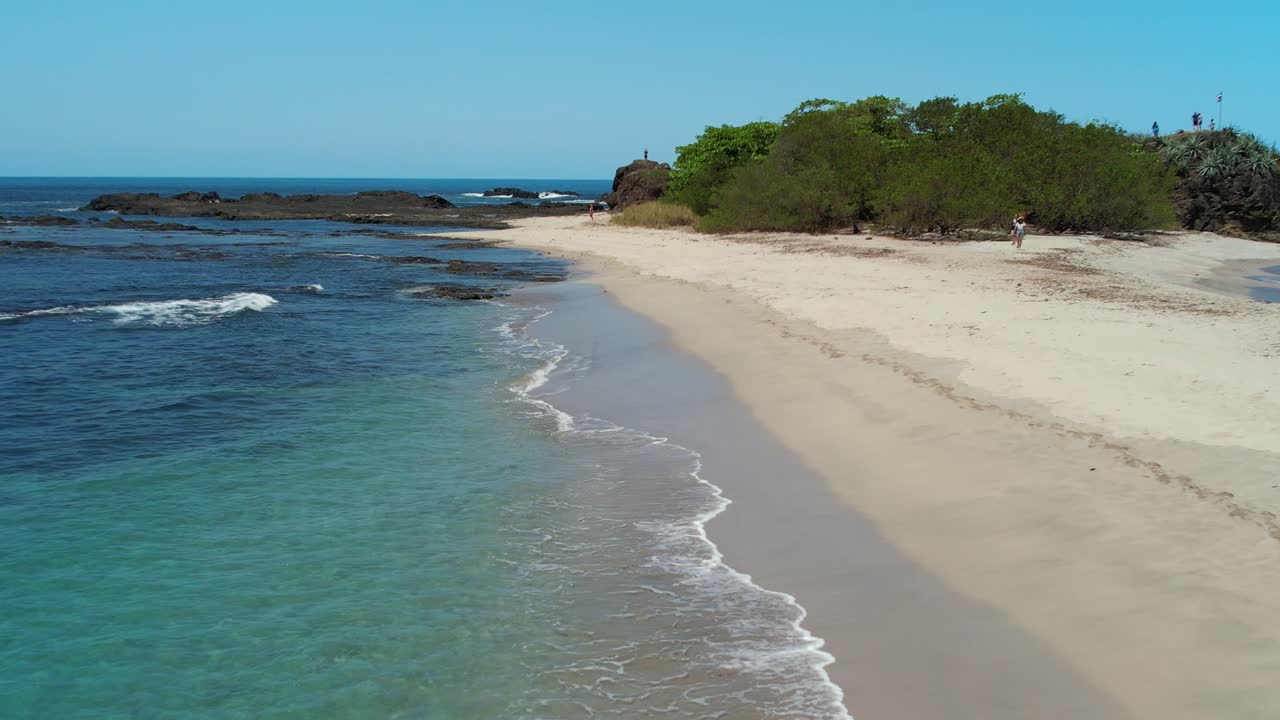 agua azul turquesa del océano con playa de arena y mujer caminando, dron aéreo de 4k costa rica