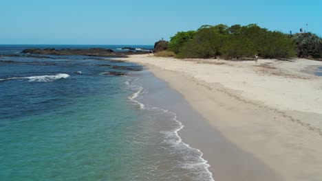 Turquoise-Blue-Ocean-Water-With-Sandy-Beach-Shore-And-Woman-Walking,-4K-Aerial-Drone-Costa-Rica