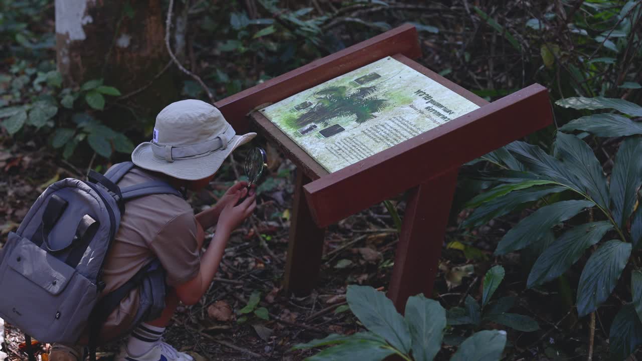 A young hiker examines a forest information board with a magnifying glass in Khao Yai