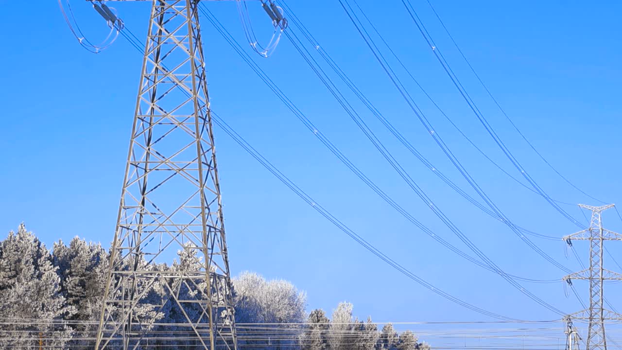 Højspændingsmast og elledninger dækket af rim og is i et sneklædt vinterlandskab mod en klar blå himmel, der viser infrastrukturen for eltransmission.