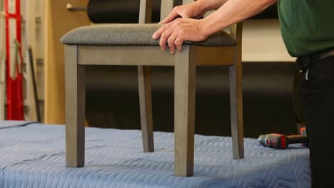 a furniture repair carpenter levels the legs on a dining chair by apply pressure to the upholstery seat